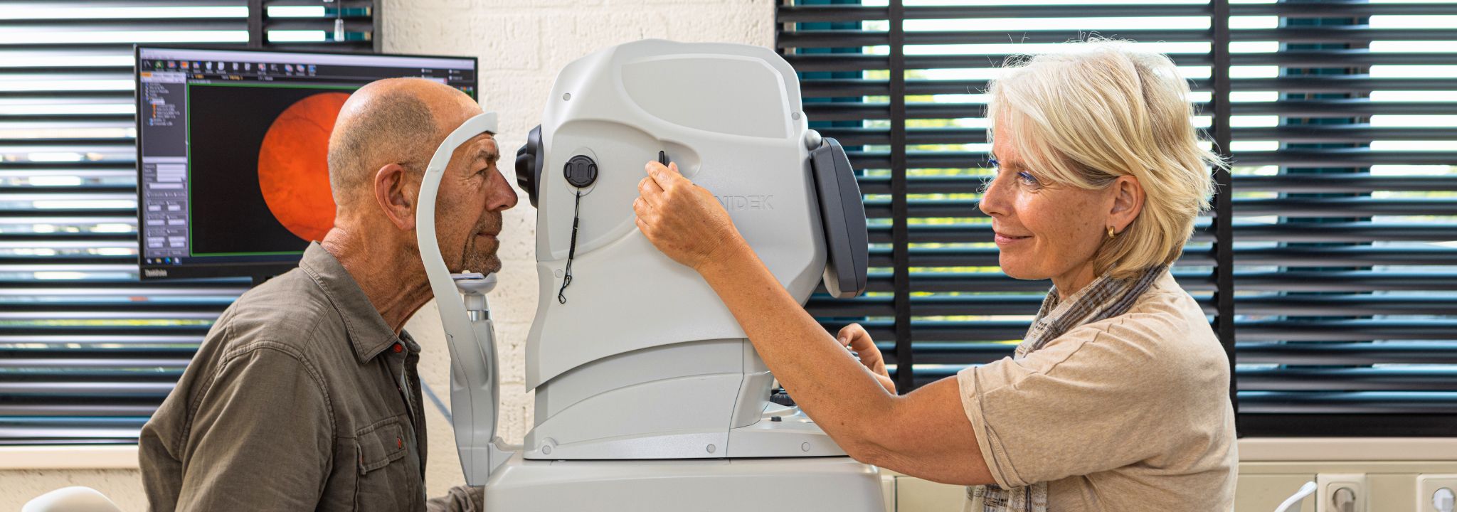 Vrouwelijke optometrist die de ogen van een oudere meneer bekijkt.